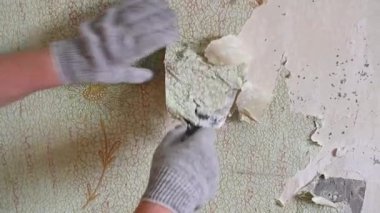 Duvardan eski duvar kağıtlarını spatula ve doğaçlama araçlarla kazımak, kendi başına bir apartman dairesini onarmak.