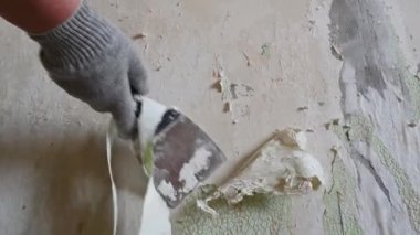 Duvardan eski duvar kağıtlarını spatula ve doğaçlama araçlarla kazımak, kendi başına bir apartman dairesini onarmak.