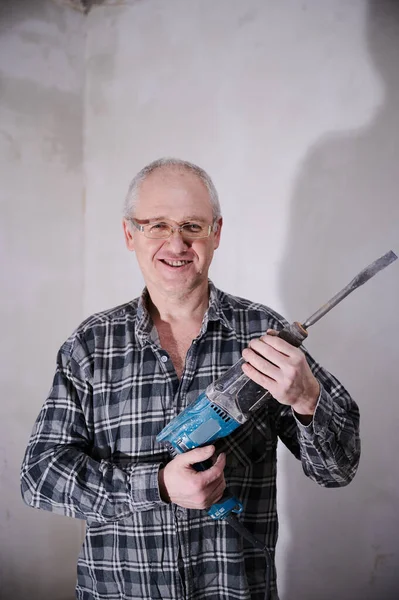 59-year-old man in glasses, a regular plaid shirt, while renovating his own apartment with a professional tool in his hands Royalty Free Stock Images