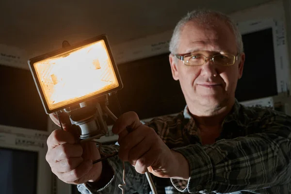 Um homem em um canteiro de obras demonstra uma lanterna que usa para iluminar o local de trabalho — Fotografia de Stock