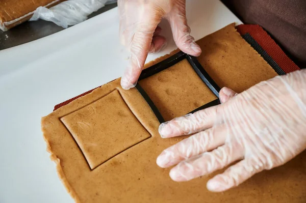 Şekerlemeci orijinal dikdörtgen kesim kullanarak zencefilli kurabiye yapar. Kadınlar koruyucu eldiven giyer. Yuvarlak hamurlu. Özel şekilli kalıplar. — Stok fotoğraf