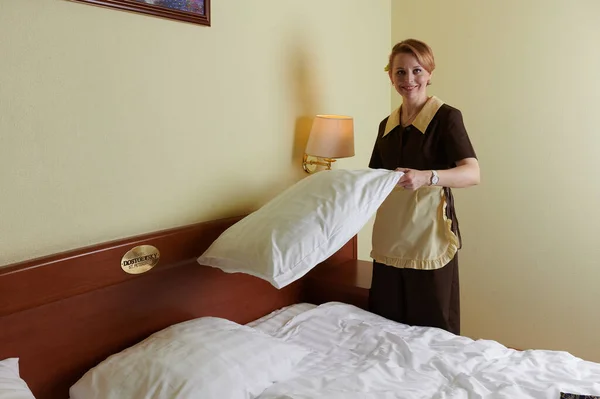 Молодая блондинка 39 лет в форме горничной отеля. Рядом с большой двуспальной кроватью. Постельное белье и постельное белье — стоковое фото