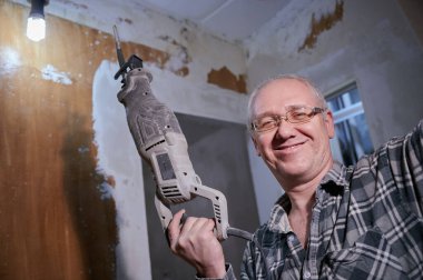 55-60 yaşlarında bir adamın portresi. Bir apartmanın tamiri sırasında kendi elleriyle, ekose gömlekli, gülümseyen, gözlük takan, bir delgi tutan bir adam.