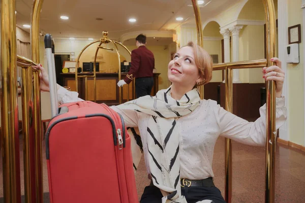 35-40-летняя женщина останавливается в отеле. Блондинка у тролля для перевозки чемоданов и багажа. В летней одежде. Она улыбается. Хорошее настроение — стоковое фото