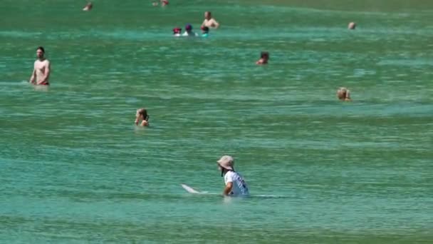 Неопознанный серфер и туристы в волнах — стоковое видео
