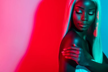 Göz kamaştırıcı, güzel bir afro kadının renkli bir arka planda izole edilmiş omuz bakımına dokunuşunun fotoğrafı.