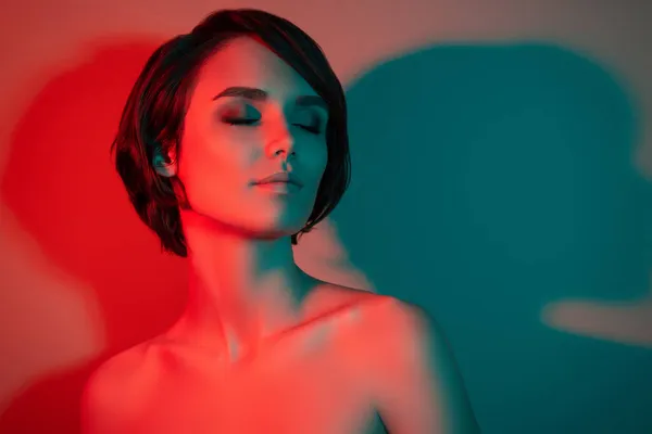 Çok çekici ve kısa saçlı bir kadının fotoğrafı. Kapalı gözler, izole edilmiş kırmızı neon ışıklı arka plan.