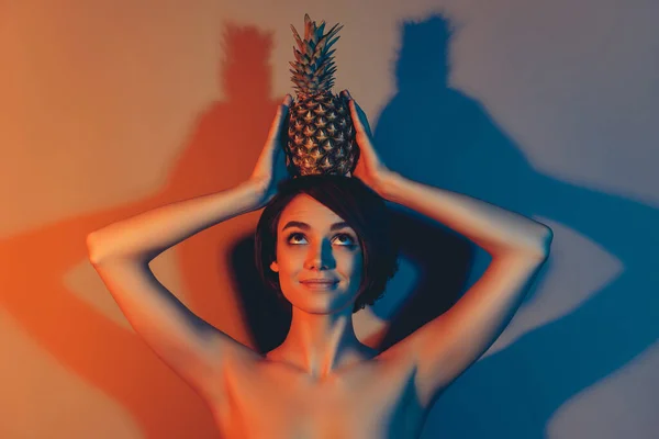 Photo de curieuse femme aux cheveux courts rêveuse tenir ananas tête regarder vide espace isolé néon lumière couleur arrière-plan — Photo