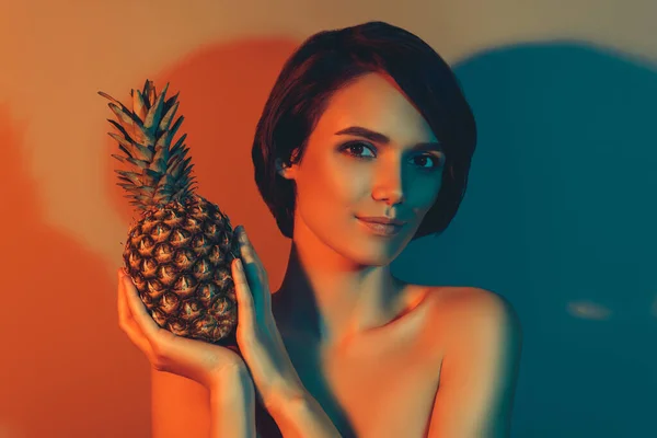 Foto de encantadora mujer de ensueño elegante celebrar fruta de piña tropical aislado naranja neón luz color fondo —  Fotos de Stock