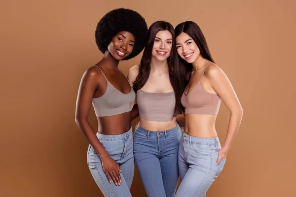 Foto van prachtige stijlvolle drie vriendinnen dragen gewas tops knuffelen glimlachen geïsoleerde beige kleur achtergrond — Stockfoto