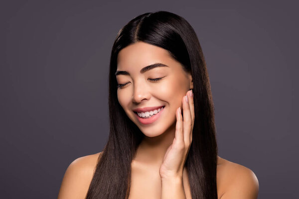 Фото веселой мечтательной китайской брюнетки женской щеки наслаждаться шелковистой гладкой кожей лица изолированный серый цвет фона