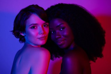 Çekici iki kadının romantik flörtleşmelerinin fotoğrafı. Canlı mor, neon rengi bir arka plan.