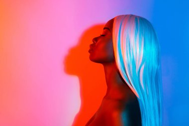 Profil tarafı genç, çarpıcı, barışçıl, gözleri kapalı, renkli arka planda yalnız bir afro kadının şehvetli fotoğrafı.