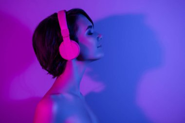 Yandan profil fotoğrafı kulaklıklı sakin kız partide müzik dinliyor izole edilmiş neon rengi arka plan kopyalama alanı