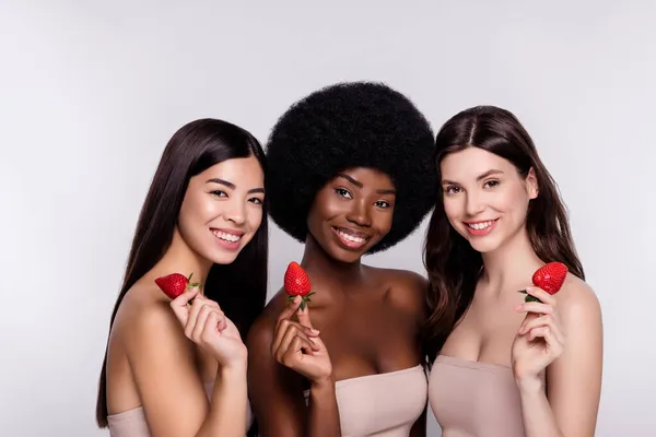 Photo de trois jeunes femmes séduisantes heureux sourire positif tenir fraise vitamines isolé sur fond de couleur grise — Photo