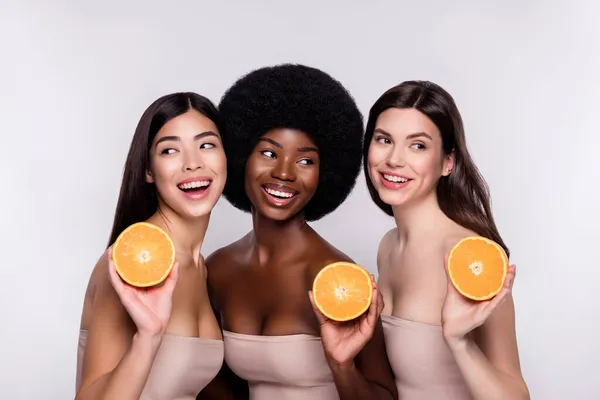 Photo trois jeunes femmes gaies heureux sourire positif vitamines orange cosmétologie isolé sur fond de couleur grise — Photo