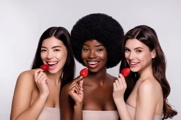 Foto van drie jonge aantrekkelijke vrouw gelukkig positief glimlach eet aardbei lekker schoonheid geïsoleerd grijs kleur achtergrond — Stockfoto