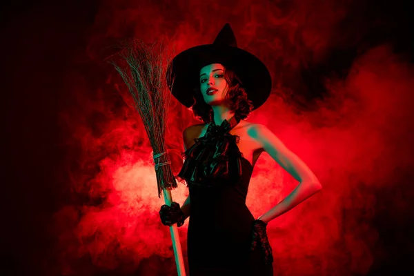 Foto del diavolo donna crudele indossare abito da strega gotico copricapo tenere mosca scopa bastone isolato rosso nebbia colore sfondo — Foto Stock