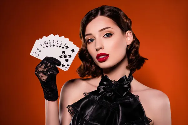 Çekici zengin ve çekici genç bir kadının el ele tutuşup poker oynadığı fotoğraf. Koyu turuncu arka planda soyutlanmış poker oynuyorlar.