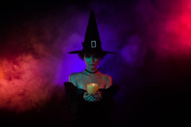 Photo of fear lady warlock doing dark sorcery necromancy hold candle flame isolated on bright mystic color background.