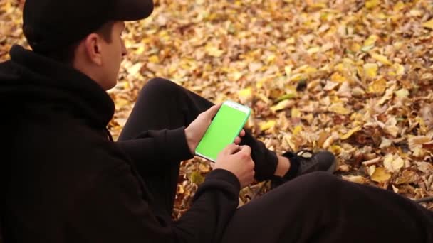Joven Está Sentado Parque Debajo Árbol Otoño Viendo Pantalla Verde — Vídeos de Stock