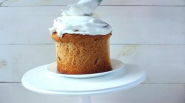 Paskalya pastası beyaz bir tabakta beyaz ahşap bir zeminde duruyor ve üzerine renkli boncuklar şeklinde bir sürü lezzetli süslemeler dökülüyor.