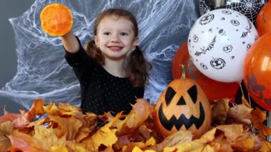 Küçük bir cadı kız Cadılar Bayramı 'nın arka planında bir dilim balkabağını ağır çekimde yerken komiktir. Cadılar Bayramı 'nın özellikleri. Balkabağından oyulmuş fener Jack-o-fener olarak bilinir.