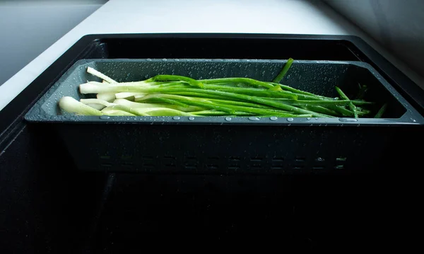 The onion feathers are washed in a special tray for vegetables. The green onions with water drops in the washing tray. Vegetable greens are good for health.