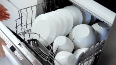 A young woman closes the dishwasher with white dishes. Build into the kitchen. Modern home kitchen. Housework. Slow motion
