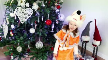 Tilki kostümü giymiş Avrupalı kıvırcık bir kız Noel ağacının yanında yavaş çekimde bir şiir anlatıyor. Yeni yıl maskeli balosu. Noel ve Yeni Yıl kavramı.