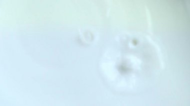 Yavaş çekimde beyaz zemin üzerine taze inek sütü dökülüyor. Yakın plan yiyecek konsepti. Beyaz sıvı damlacıklar düşer..