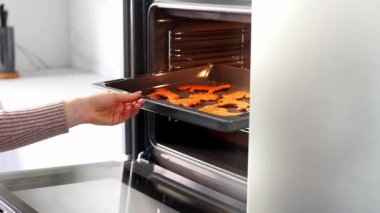 Kadının elleri fırını açıyor ve fırına zencefilli bisküviler koyuyor. Beyaz, modern bir mutfakta fırında yemek pişiren genç bir kadın. Noel ve Yeni Yıl kavramı