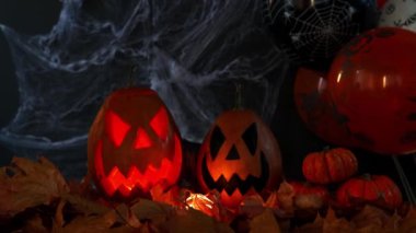 Örümcek ağları, sonbahar yaprakları ve balonları olan siyah bir zemin üzerinde Jack-o-fener olarak bilinen balkabağından oyulmuş fener. Cadılar Bayramı 'nın özellikleri. Şaka mı şeker mi?