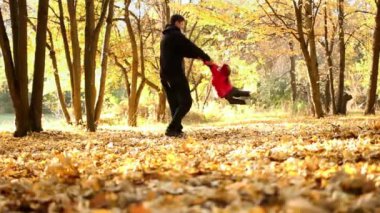 Dad swirles small daughter for the hands in an autumn park against a backdrop of trees and fallen yellow leaves