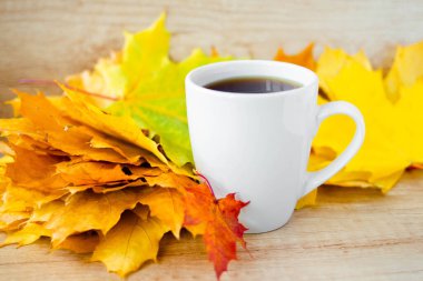 White cup of tea and autumn maple leaves on wooden background. The concept of calm, relaxation and autumn. Autumn background.