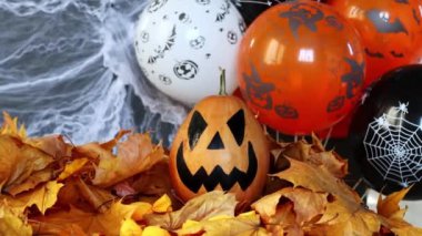 Halloweens holiday attributes. Lantern carved from pumpkin known as Jack-o-lantern on a black background with spider webs, autumn leaves and balloons. Trick or treat.