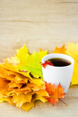 White cup of tea and autumn maple leaves on wooden background. The concept of calm, relaxation and autumn. Autumn vertical background.