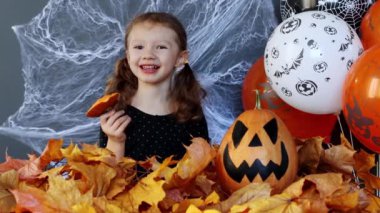 Küçük bir cadı kız Cadılar Bayramı 'nın arka planında bir dilim balkabağını ağır çekimde yerken komiktir. Cadılar Bayramı 'nın özellikleri. Balkabağından oyulmuş fener Jack-o-fener olarak bilinir..