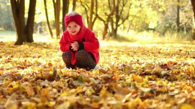 The cute little girl in the red coat is throwing yellow fallen autumn leaves up, while having fun and playing outdoors in the fall season. Child tossing colorful autumn foliage up in the air in the park