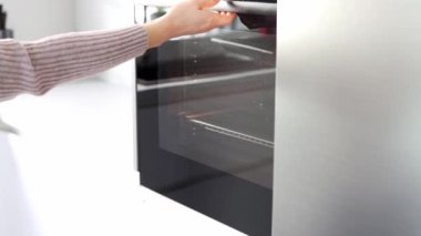 Kadının elleri fırını açıyor ve fırına zencefilli bisküviler koyuyor. Beyaz, modern bir mutfakta fırında yemek pişiren genç bir kadın. Noel ve Yeni Yıl kavramı