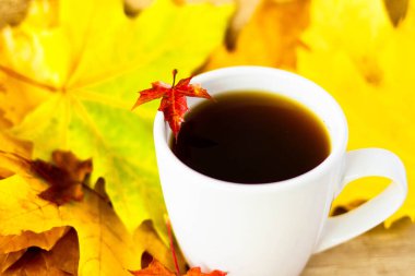 White cup of tea and autumn maple leaves on wooden background. The concept of calm, relaxation and autumn. Autumn background.