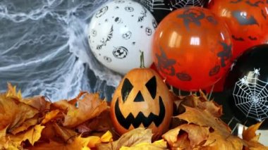 Halloweens holiday attributes. Lantern carved from pumpkin known as Jack-o-lantern on a black background with spider webs, autumn leaves and balloons. Trick or treat.