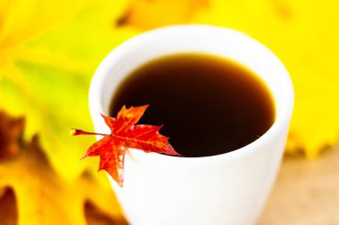 White cup of tea and autumn maple leaves on wooden background. The concept of calm, relaxation and autumn. Autumn background.