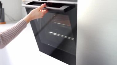 Kadınlar fırını açarlar ve fırından ağır çekimde bir çarşaf çıkarırlar. Beyaz, modern bir mutfakta fırında yemek pişiren genç bir kadın. Noel ve Yeni Yıl kavramı.