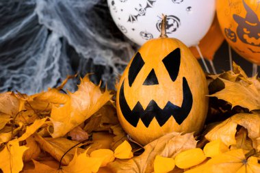 Cadılar Bayramı 'nın özellikleri. Örümcek ağları, sonbahar yaprakları ve balonları olan siyah bir zemin üzerinde Jack-o-fener olarak bilinen balkabağından oyulmuş fener. Şaka mı şeker mi?.