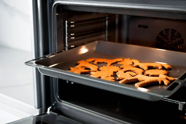 Close up Christmas gingerbread on a baking sheet in open modern oven in a bright kitchen. Christmas cookies in the oven - warm light, festive atmosphere. Concept of winter, Christmas, and New Year.