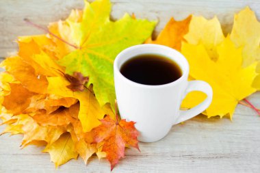 White cup of tea and autumn maple leaves on wooden background. The concept of calm, relaxation and autumn. Autumn background.