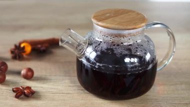 Fragrant black tea is brewed in a glass teapot on a wooden background decorated with nuts and spices. Concept of Christmas and New Year.