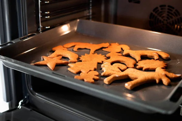 Close up Christmas gingerbread on a baking sheet in open modern oven in a bright kitchen. Christmas cookies in the oven - warm light, festive atmosphere. Concept of winter, Christmas, and New Year.