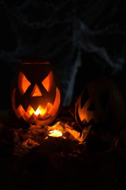 Halloween's holiday attributes. Lantern carved from pumpkin known as Jack-o-lantern glow in the dark on a black background with spider webs, autumn leaves and balloons. Trick or treat.